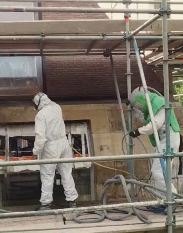 Medewerkers behandelen kalkstenen buitenwand vanaf een steiger